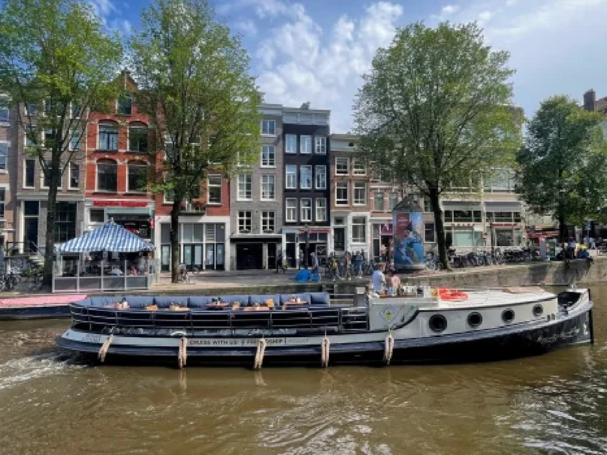a boat floating along a river next to a body of water with Anne Frank House in the background