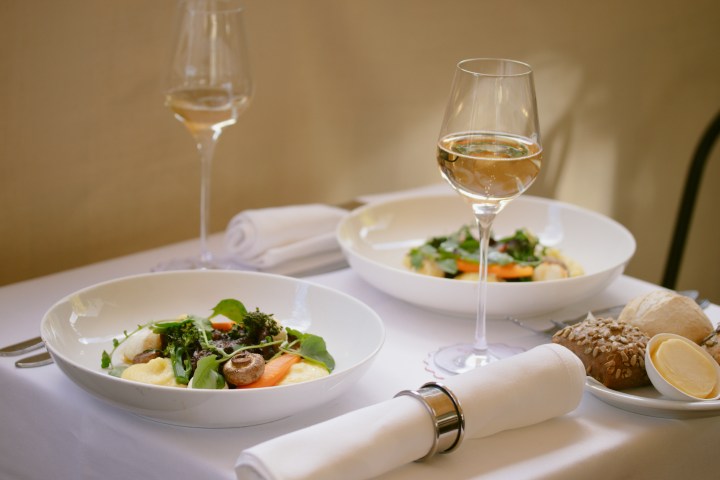 Elegant table set for two with plates of salad and glasses of white wine.