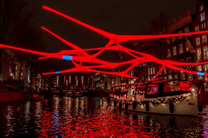 Boat under glowing red light art installation over a canal at night.
