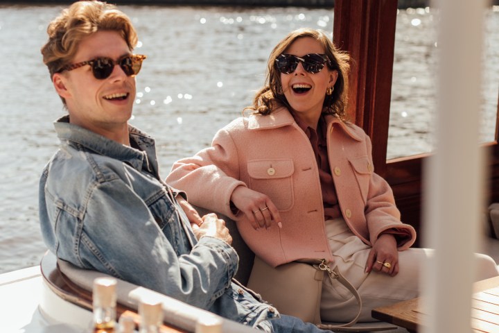 Man and woman in sunglasses laughing on a boat with bottles in the foreground.