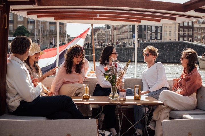 Group of people sitting on a boat, talking and relaxing with a Dutch flag in the background.