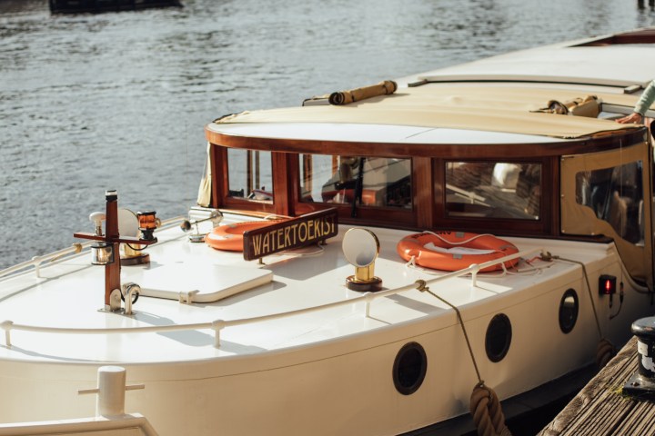 White boat docked by wooden pier with cityscape and bridge in background.