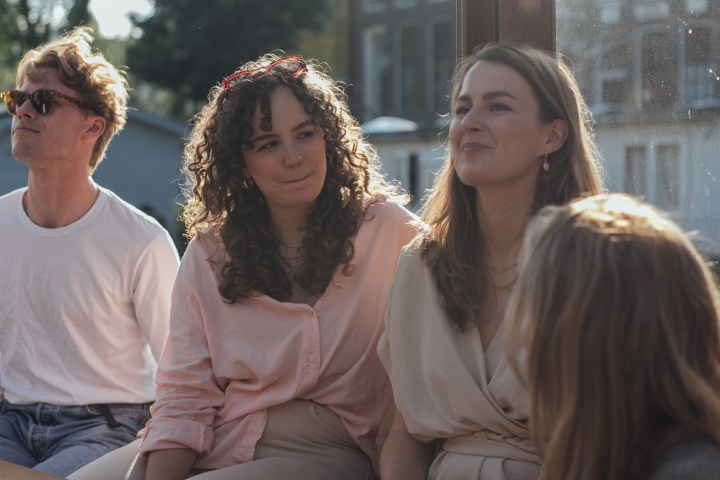 Group of four people sitting together in sunlight, smiling and talking indoors.