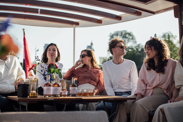 Group of people sitting on a boat with bottles and glasses on the table.