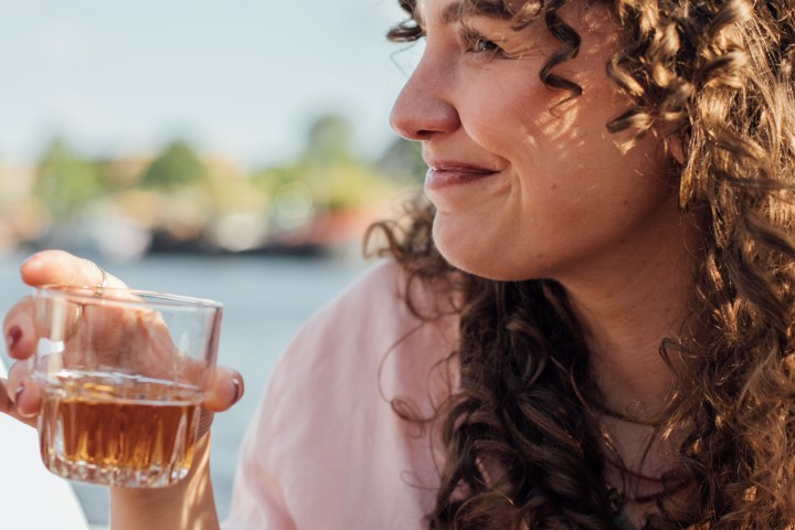 Woman in pink shirt with curly hair holding a drink outdoors.