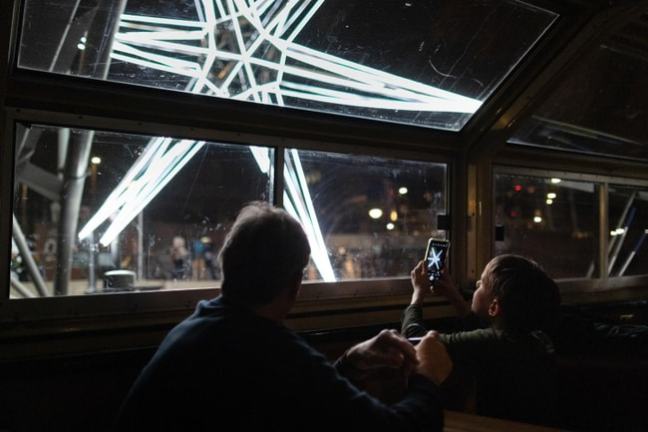 Person and child inside, looking at glowing star outside the window in the evening.