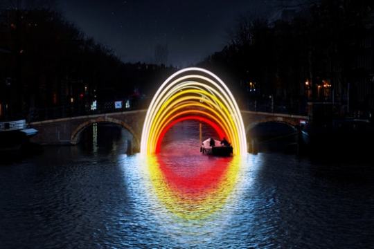 Boat under rainbow-shaped lights on a canal at night.