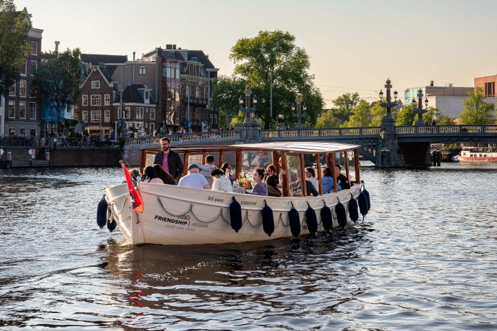 Boat with people on canal near bridge and buildings under a clear sky.