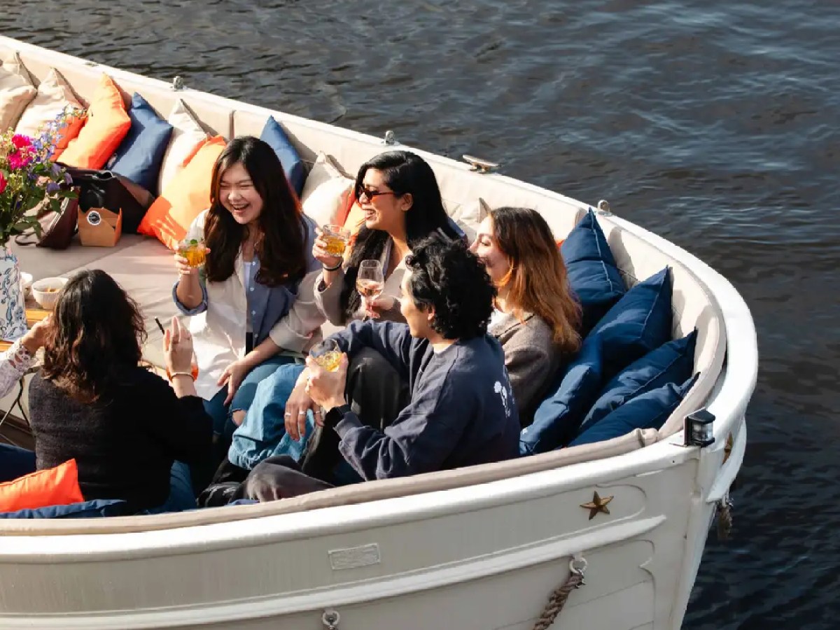 People sitting in a boat on water, holding drinks and smiling.