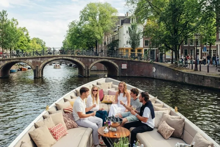 People relaxing on a boat in a canal with a bridge and trees in the background.